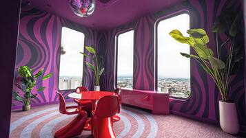 A room with a red table and chairs, large windows, and potted plants.