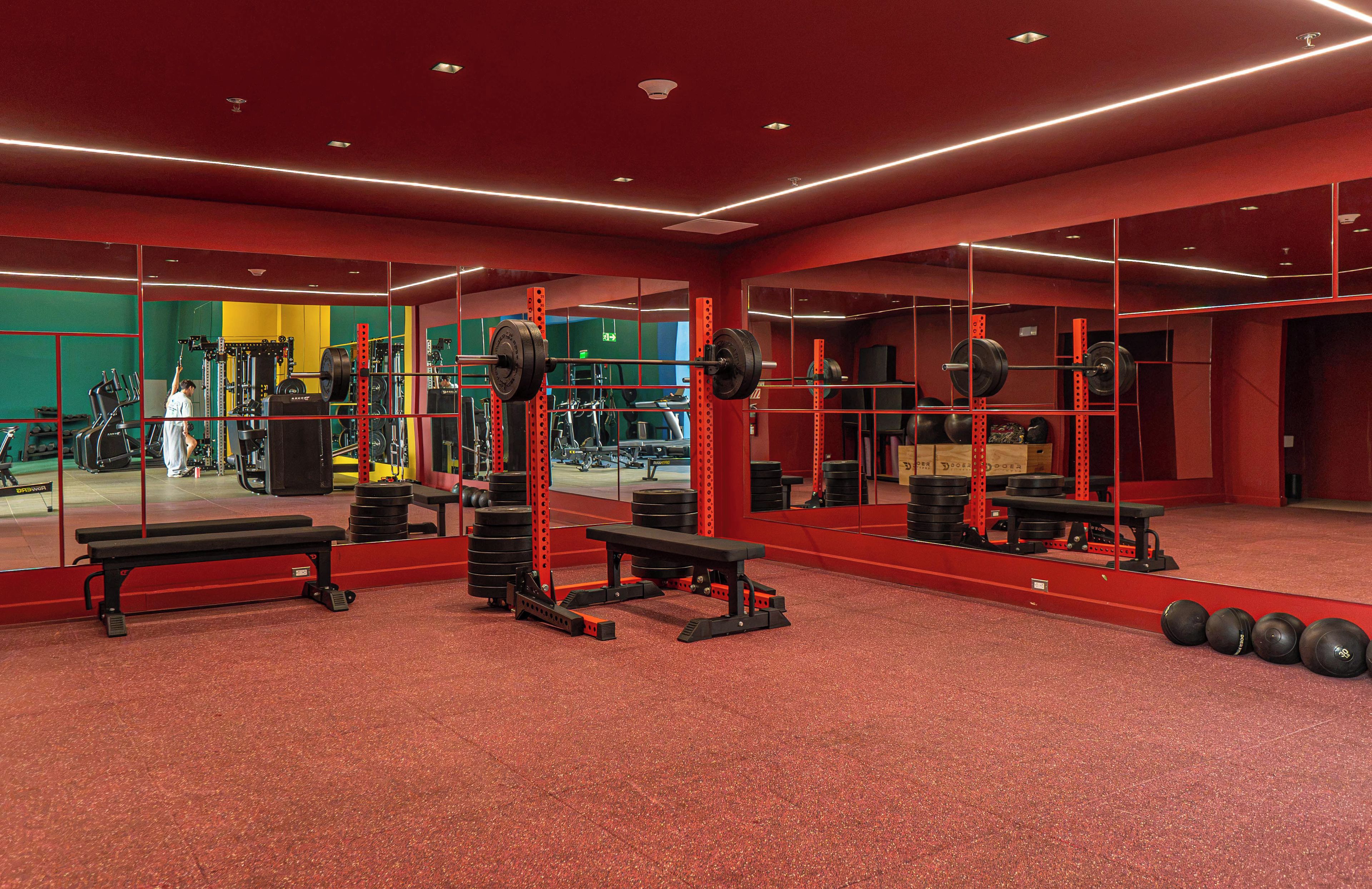 Un gimnasio con paredes rojas, espejos y diverso equipamiento de ejercicio.