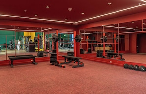 Un gimnasio con paredes rojas, espejos y diverso equipamiento de ejercicio.