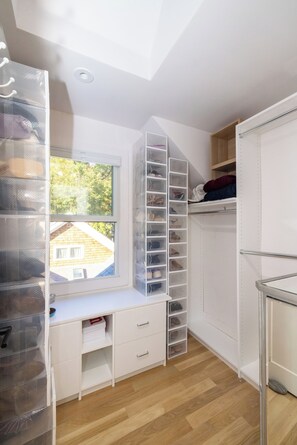 Quarto com escrivaninha embutida, espaço para guardar sapatos e janela com vista para uma casa.