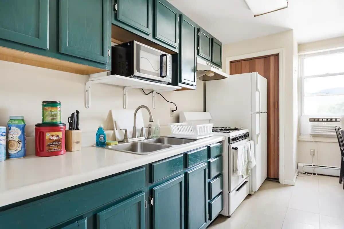 A kitchen with teal cabinets, a microwave, a stove, and a refrigerator.