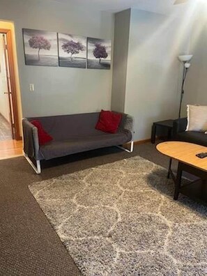 Een woonkamer met een grijze bank, een houten salontafel en een vloerkleed met een patroon.