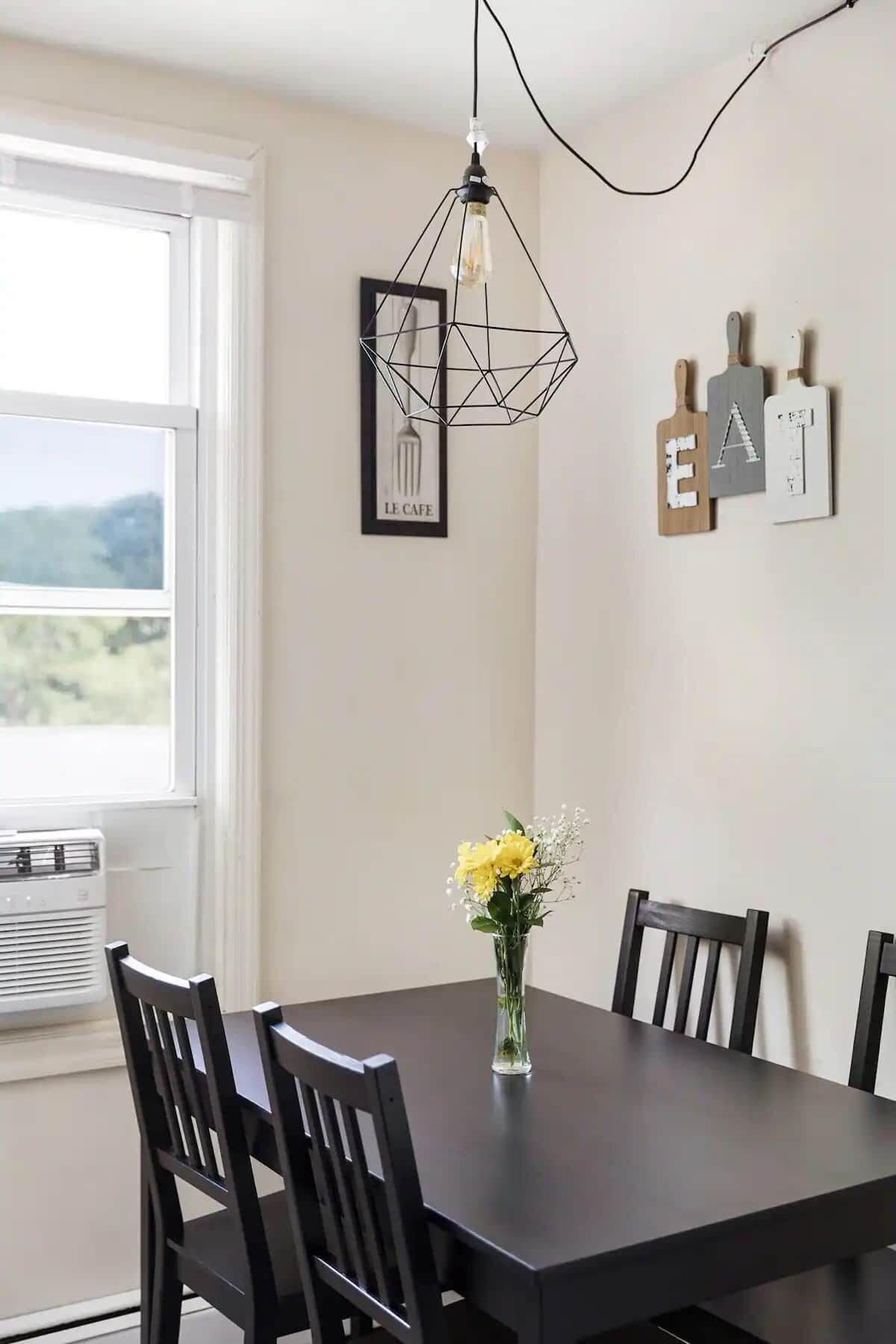 Un espace repas comprenant une table, des chaises, un vase avec des fleurs, un luminaire suspendu et des éléments de décoration murale.