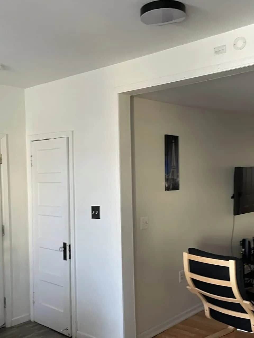 A room with a white door, a small framed picture on the wall, and a wooden chair.
