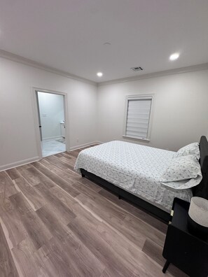 Een slaapkamer met een bed, een deur, een raam en een lamp.