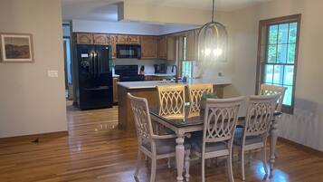 A kitchen with wooden cabinets, a black refrigerator, and a dining area with a glass table and white chairs.