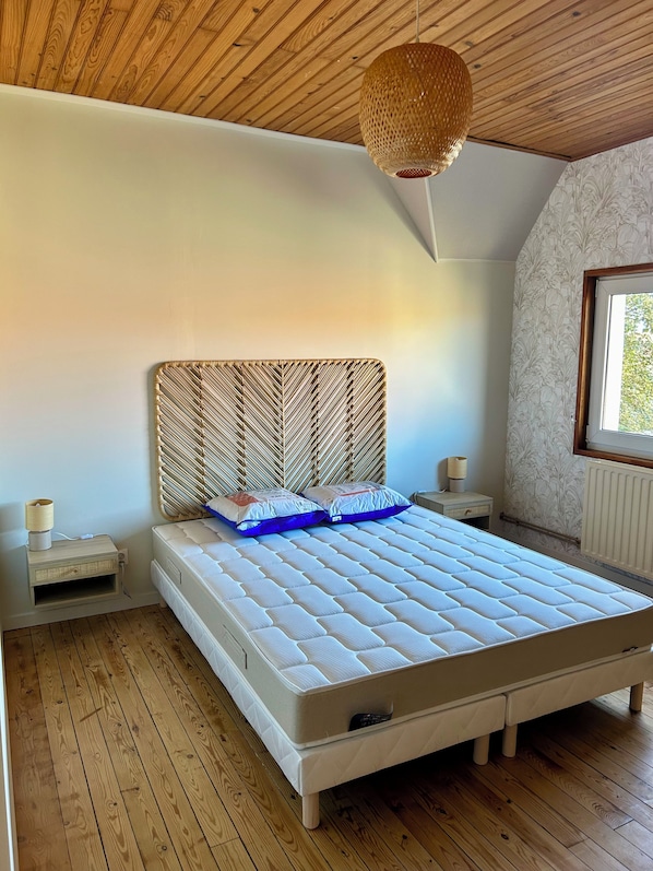 Ein Schlafzimmer mit Holzboden, einem Bett mit gewebtem Kopfteil, einem Nachttisch mit Lampe und einem Fenster mit Blick.