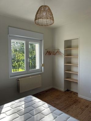 Ein Zimmer mit Fenster, Heizkörper, Holzboden und einer Pendelleuchte.