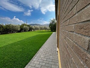 A paved pathway leading to a brick wall, with a green lawn and trees in the background. - New Listing (Villa Musone)