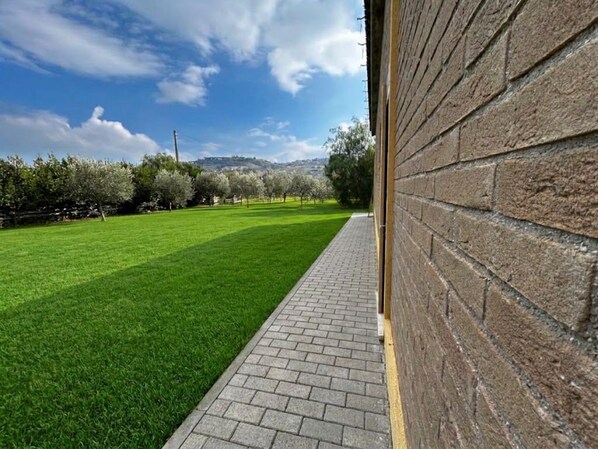 A paved pathway leading to a brick wall, with a green lawn and trees in the background. - New Listing (Villa Musone)