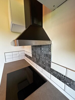 Cozinha com coifa de aço inoxidável, painel de backsplash estampado e bancada branca.