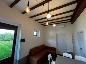 A room with a brown sofa, a dining table with chairs, a ceiling with exposed beams, and a door. - New Listing (Villa Musone)