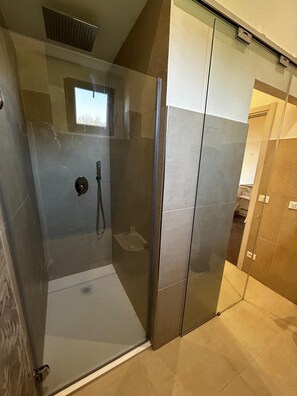 A glass-enclosed shower stall with a handheld showerhead and a small window above. - New Listing (Villa Musone)