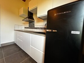 Cozinha com armários brancos, geladeira preta e painel decorativo atrás do fogão.