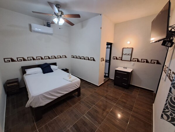 A hotel room with a bed, a nightstand, a ceiling fan, an air conditioning unit, a bathroom with a sink and mirror, and decorative wall patterns. - New Listing (Brisas de Zicatela)