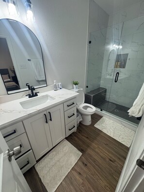 A modern bathroom with a white vanity, a large mirror, a glass shower enclosure, and a white toilet. - Spacious 4-bedroom townhome in soothing Fort Worth with AC (Fort Worth)