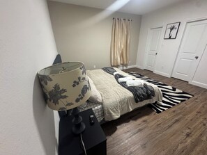 A bedroom with a bed, a lamp, a remote control, a zebra-patterned rug, and a door. - Spacious 4-bedroom townhome in soothing Fort Worth with AC (Fort Worth)
