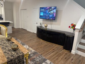 A modern living room with a flat-screen TV mounted on the wall, a black console table, a patterned rug, and a staircase to the right. - Spacious 4-bedroom townhome in soothing Fort Worth with AC (Fort Worth)