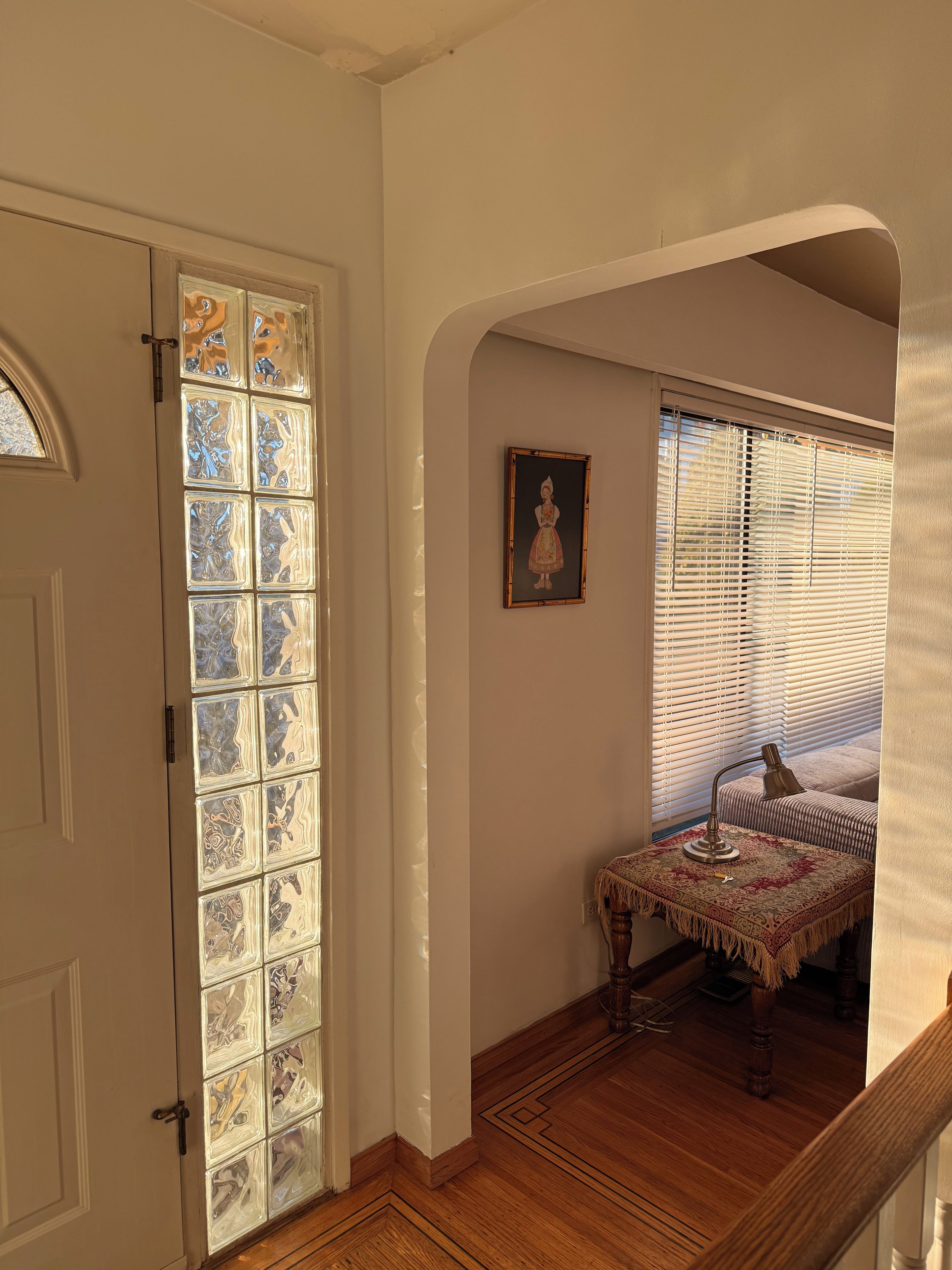 A hallway with a door leading to a room with a patterned glass door, a framed picture on the wall, and a table with a lamp.