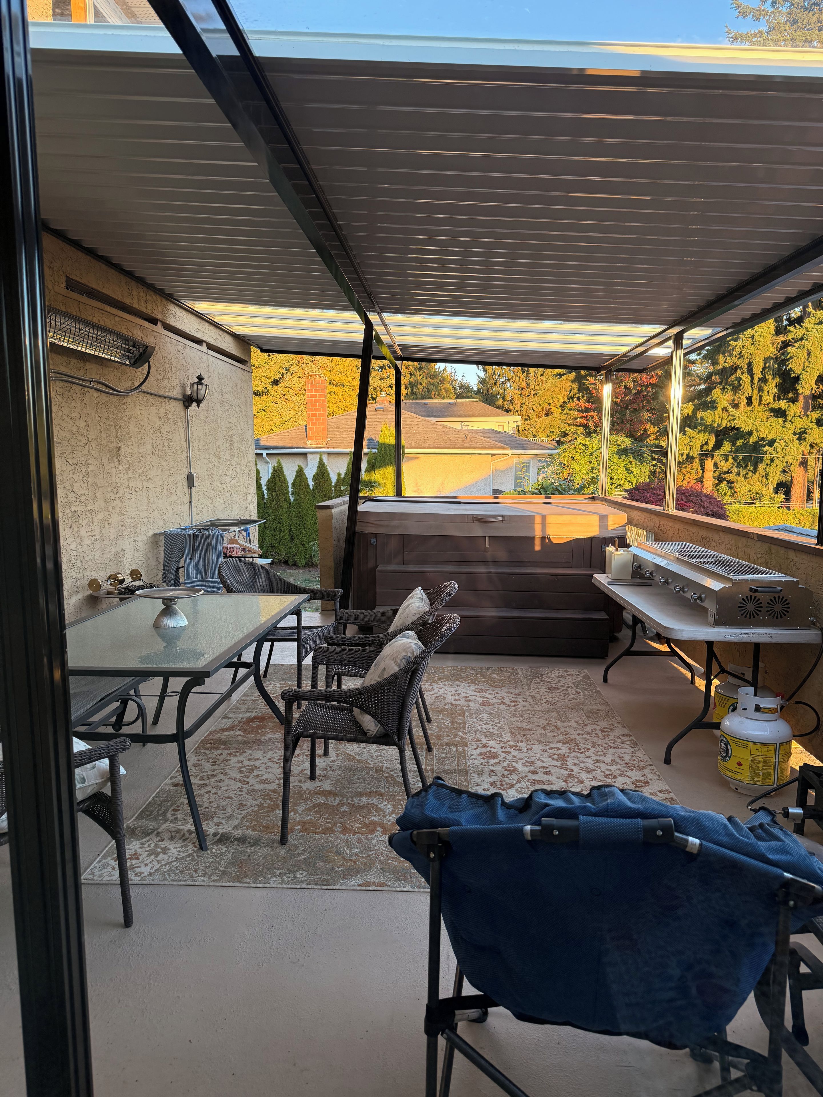 An outdoor patio with a covered seating area, a grill, and a view of the neighborhood.