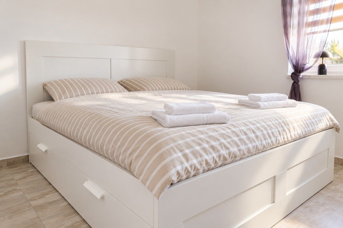 Ein Bett mit Kopfteil, zwei Kissen, einer gestreiften Tagesdecke und zwei gefalteten Handtüchern.