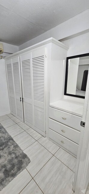 Un dormitorio con un armario blanco, un tocador con cajones y un espejo.