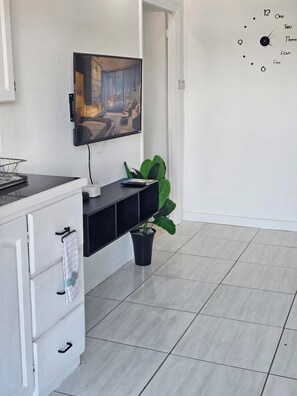 Una sala de estar moderna con un televisor de pantalla plana montado en la pared, un mueble de entretenimiento negro debajo y una planta en maceta en el suelo.