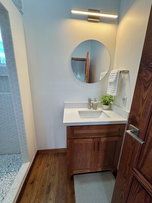 A bathroom with a white sink, wooden cabinets, a round mirror, and a towel rack. - Private Home + FREE Jaguar Reef Resort Access (Hopkins)