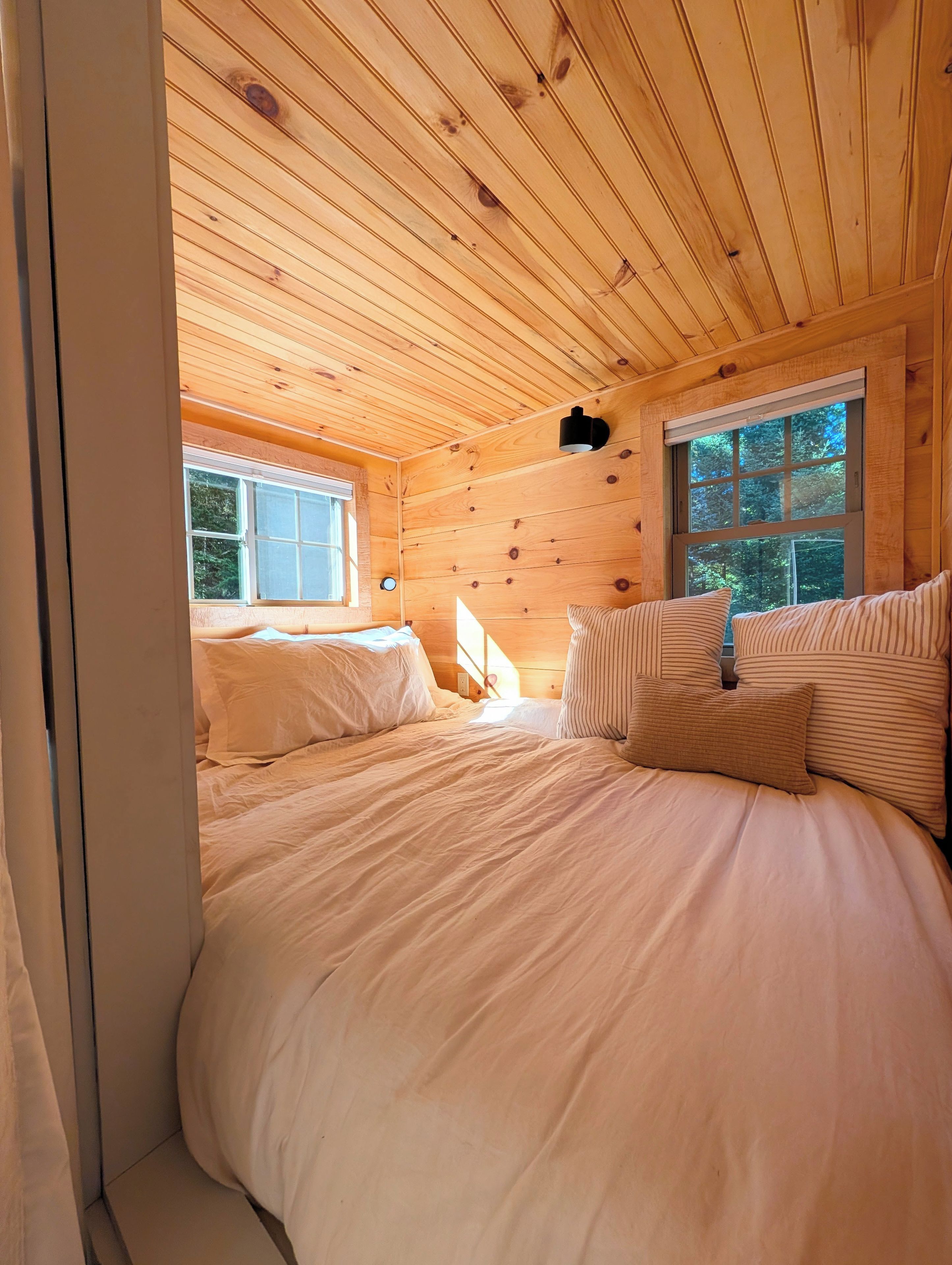 Ein Schlafzimmer einer Holzhütte mit zwei Betten, einem Fenster und einer Wandleuchte.