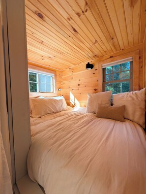 A wooden cabin bedroom with two beds, a window, and a wall-mounted light fixture. - Tiny House Woodland Retreat • Private Hot Tub • Sugarbush (Warren)