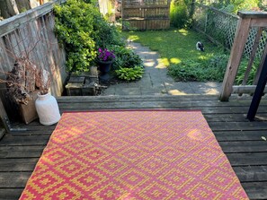 Een houten terras met een kamerplant, een patroonkleed en een houten omheining.
