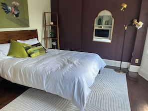 Une chambre à coucher avec un lit, une lampe de chevet, un miroir et une étagère fixée au mur.