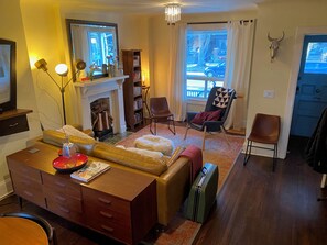 Un salon chaleureux avec une cheminée, une bibliothèque, un canapé confortable et une vue sur la rue.