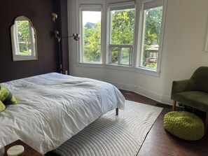 Een slaapkamer met een bed, een raam, een lamp en een stoel.