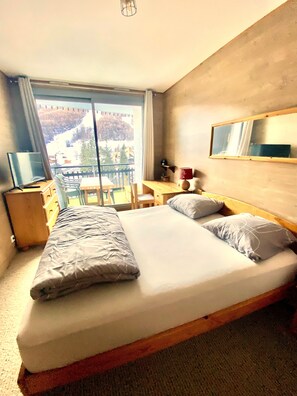 Ein Hotelzimmer mit einem Bett, einem Schreibtisch, einem Sessel, einem Fernseher und Blick auf eine verschneite Landschaft.