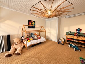 Een kinderkamer met een houten bedframe, een hanglamp, een radiator, een speelgoedauto en een plank met speelgoed.