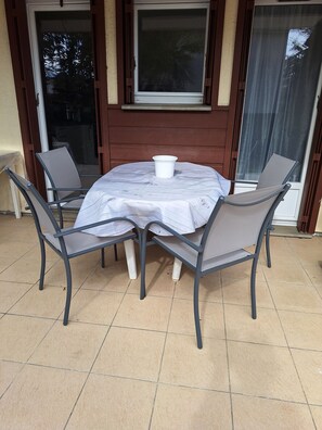 Une table ronde recouverte d’une nappe blanche, entourée de quatre chaises en métal dont les dossiers sont en treillis.