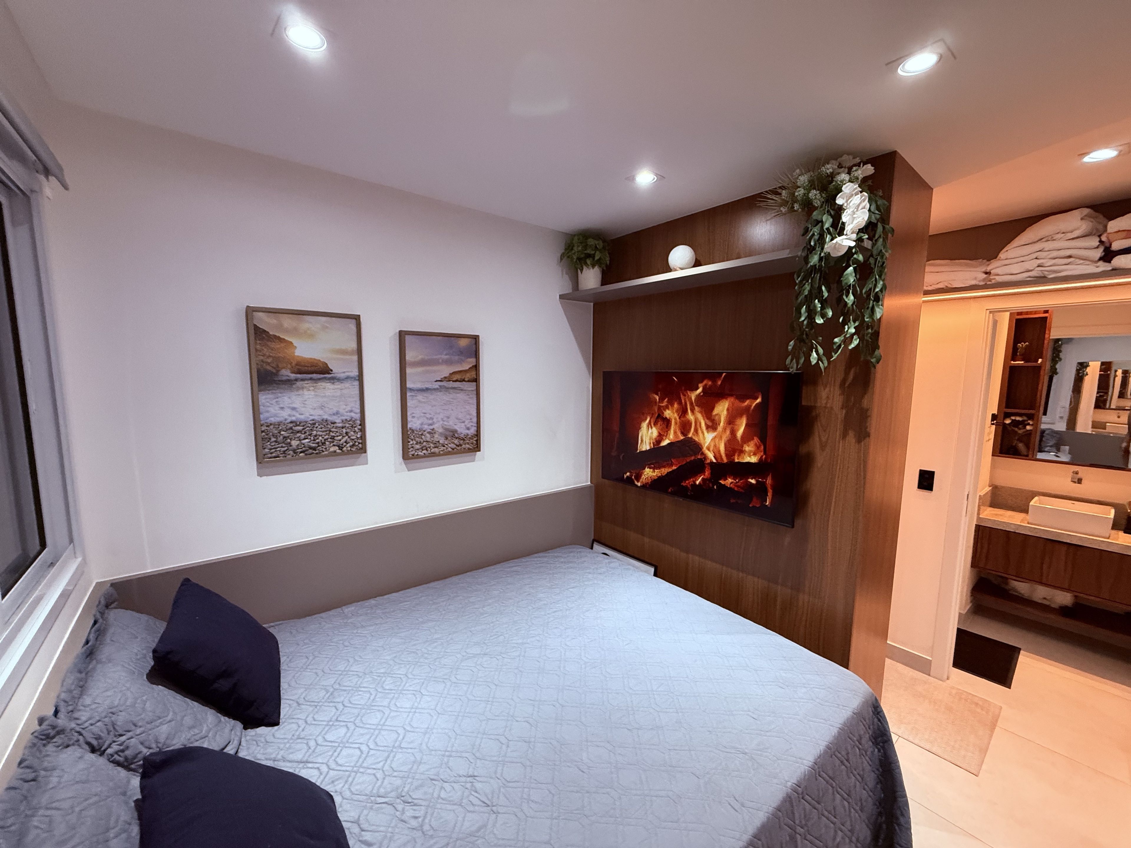 A bedroom with a bed, a wall-mounted TV, and a fireplace.
