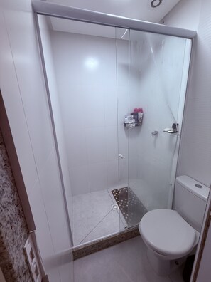 Un baño con ducha de vidrio, inodoro y un estante con artículos de aseo.