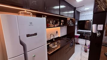 A modern kitchen with a white refrigerator, stainless steel appliances, and dark cabinetry.