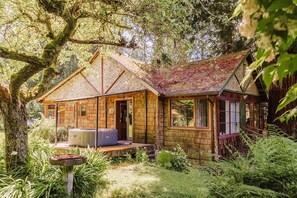 A rustic wooden cabin with a porch, surrounded by dense greenery and trees. - Vintage charm, giant yard & hot tub in "The Creek" (Roberts Creek)