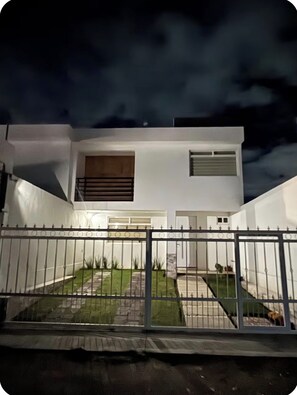 Una moderna casa a due piani con facciata bianca, un cancello per garage e un vialetto recintato.