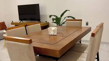 Un comedor con una larga mesa de madera, seis sillas tapizadas, un televisor y una planta en maceta.