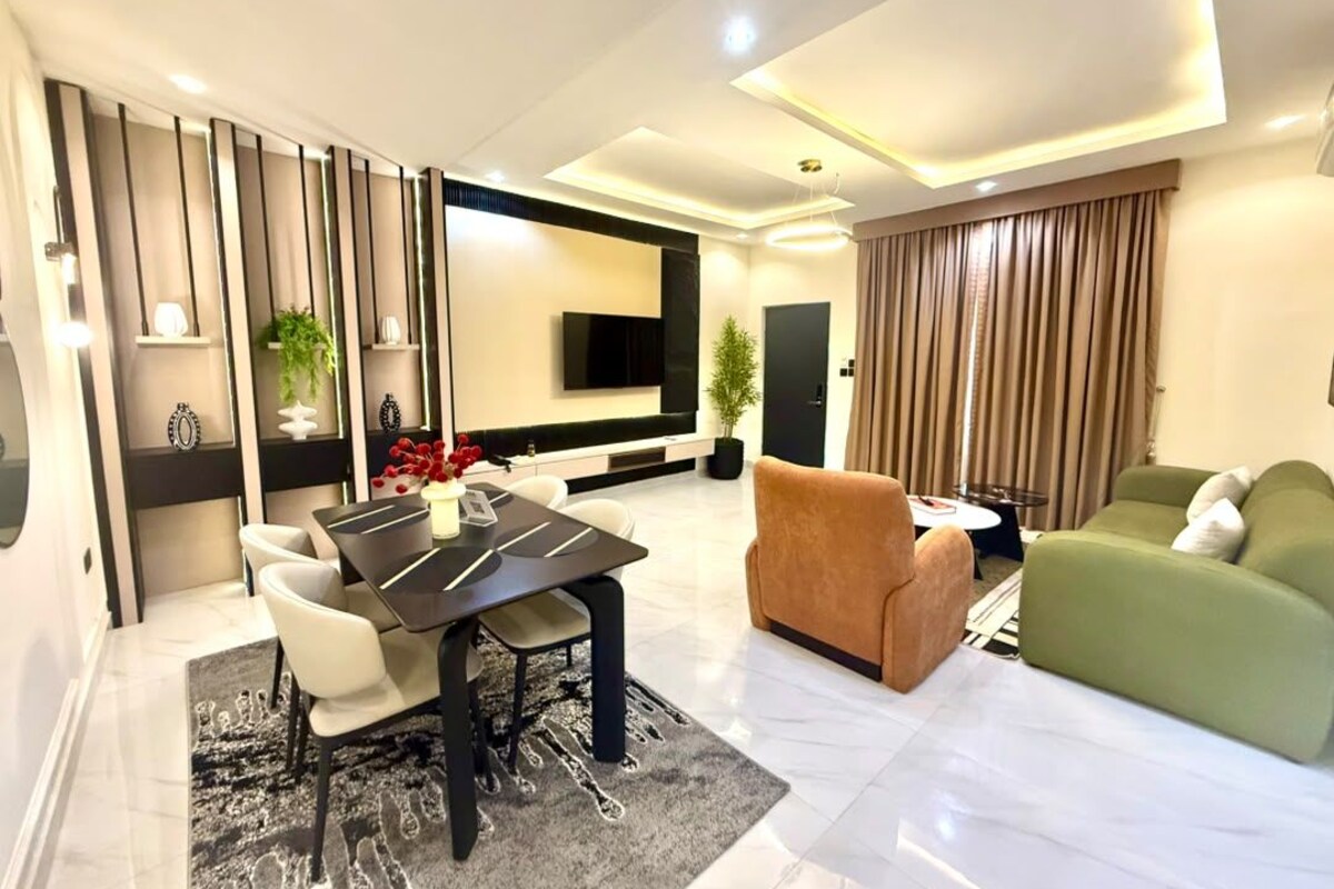 Een moderne woonkamer met een eetgedeelte, een groene bank en een flatscreen televisie aan de muur.