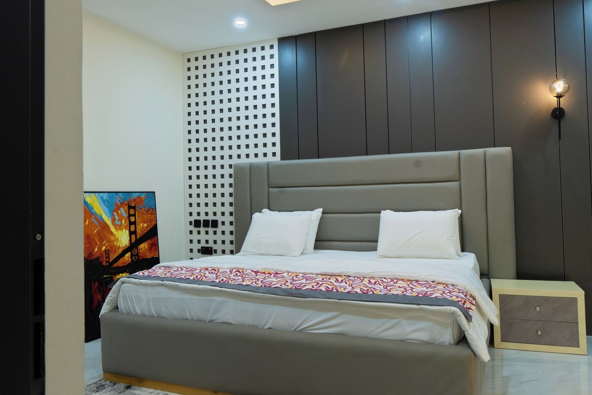 Een moderne slaapkamer met een groot bed, een kamerkleed met patroon, een wandlamp en een plafondlamp.