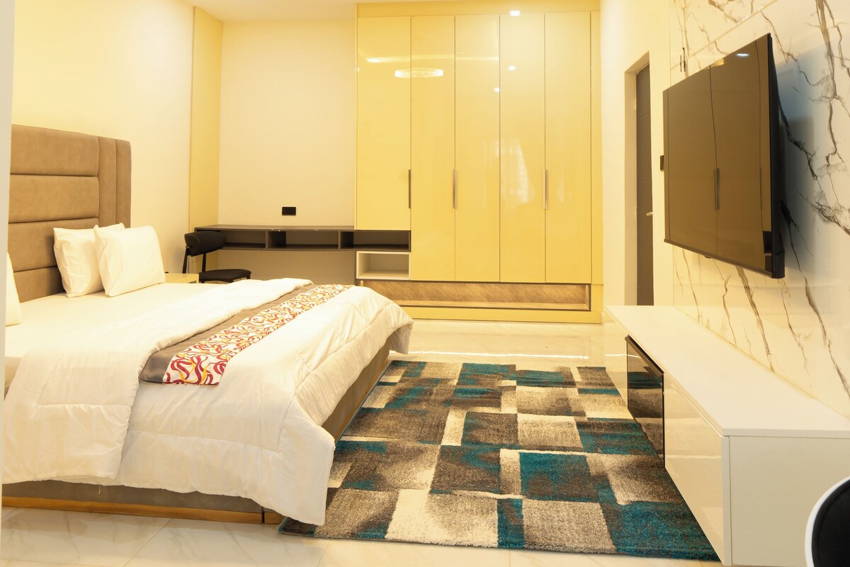 Een moderne slaapkamer met een bed, een bureau, een kledingkast en een aan de muur bevestigde televisie.