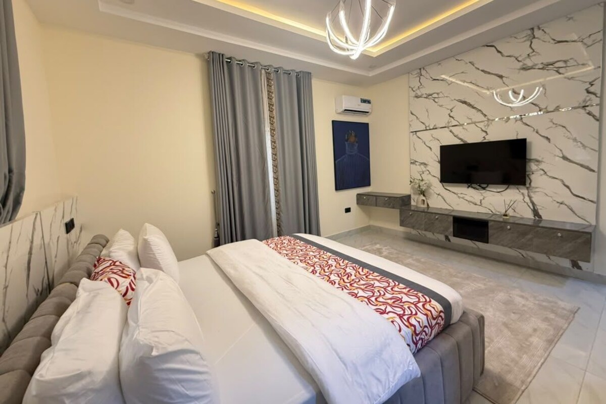 Een moderne slaapkamer met een bed, een aan een marmeren muur bevestigde televisie en een plafondlamp.