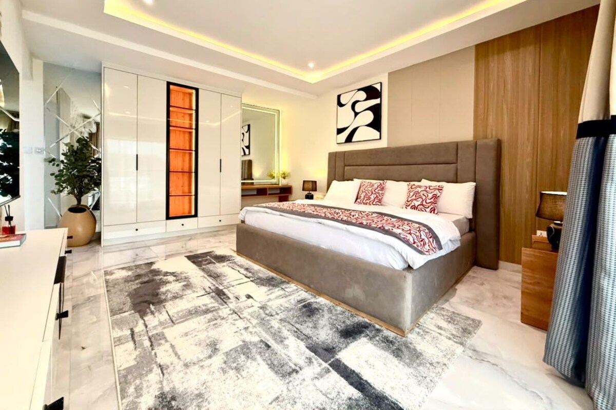 Een moderne slaapkamer met een groot bed, een kledingkast, een spiegel en een schilderij aan de muur.