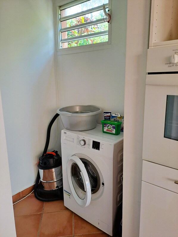 Un espace réduit dédié à la buanderie, comprenant un lave-linge, un étendoir et un aspirateur.