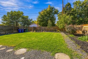 A backyard with a well-maintained lawn, a wooden fence, a shed, and a small garden area with various plants. - Spacious Furnished 5BR Denver Home, Pet-Friendly, Fenced Yard & Garage (Denver)